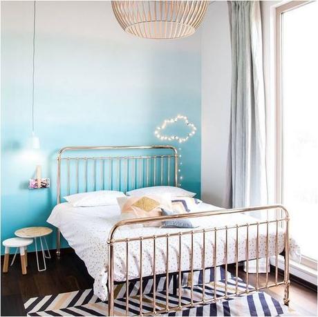 Chambre d'ado avec un lit en fer forgé de couleur cuivre, mur tie and dye bleu, suspension en guise de lampe de chevet, nuage en guirlande lumineuse au mur, et grande suspension au milieu de la pièce